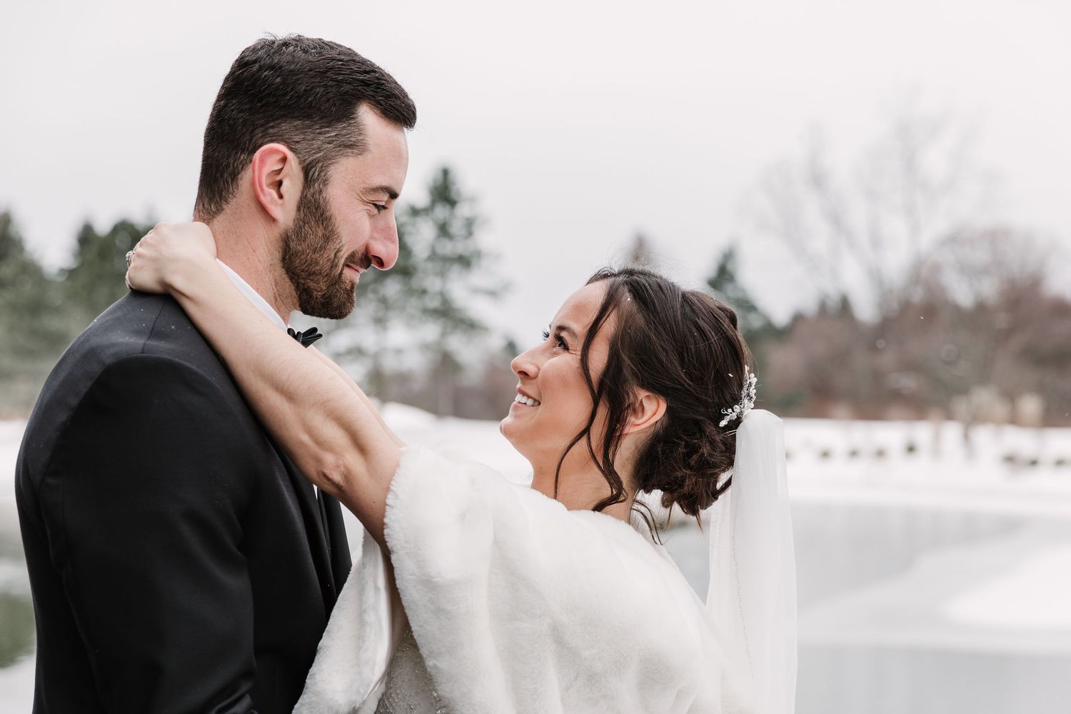 A romantic winter wedding photoshoot with a couple embracing in front of snowy scenery.