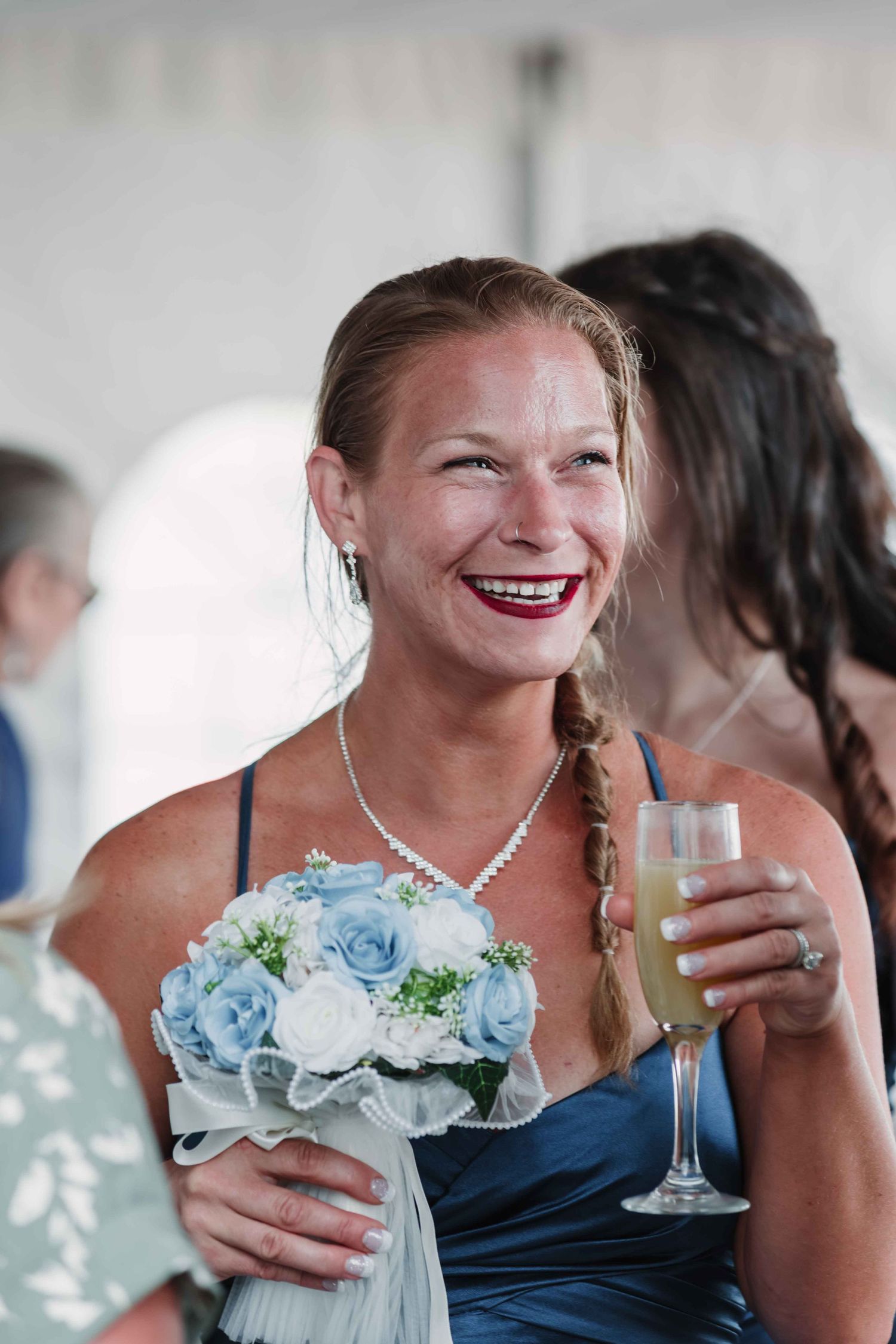 Bridesmaid in navy dress laughs while holding a champagne glass at reception.