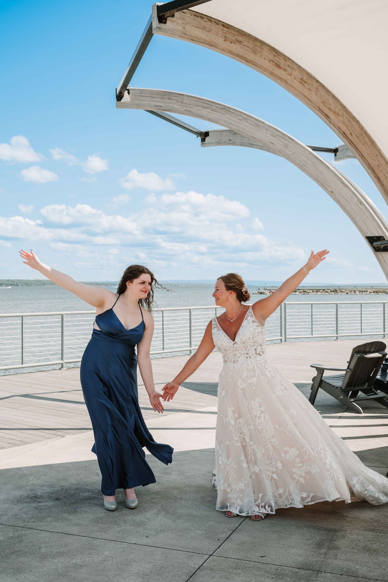 Two people in contrasting outfits dance and pose dramatically on a seaside deck.
