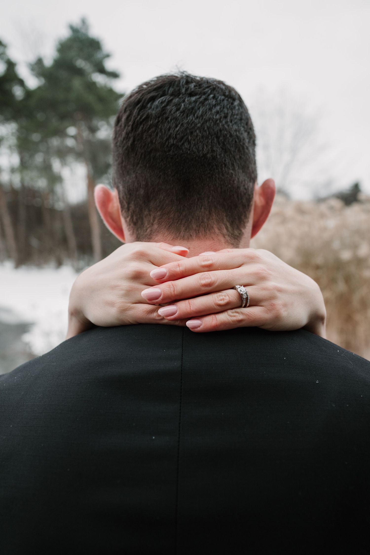 Close-up of hands resting on groom's suit jacket showing wedding ring.