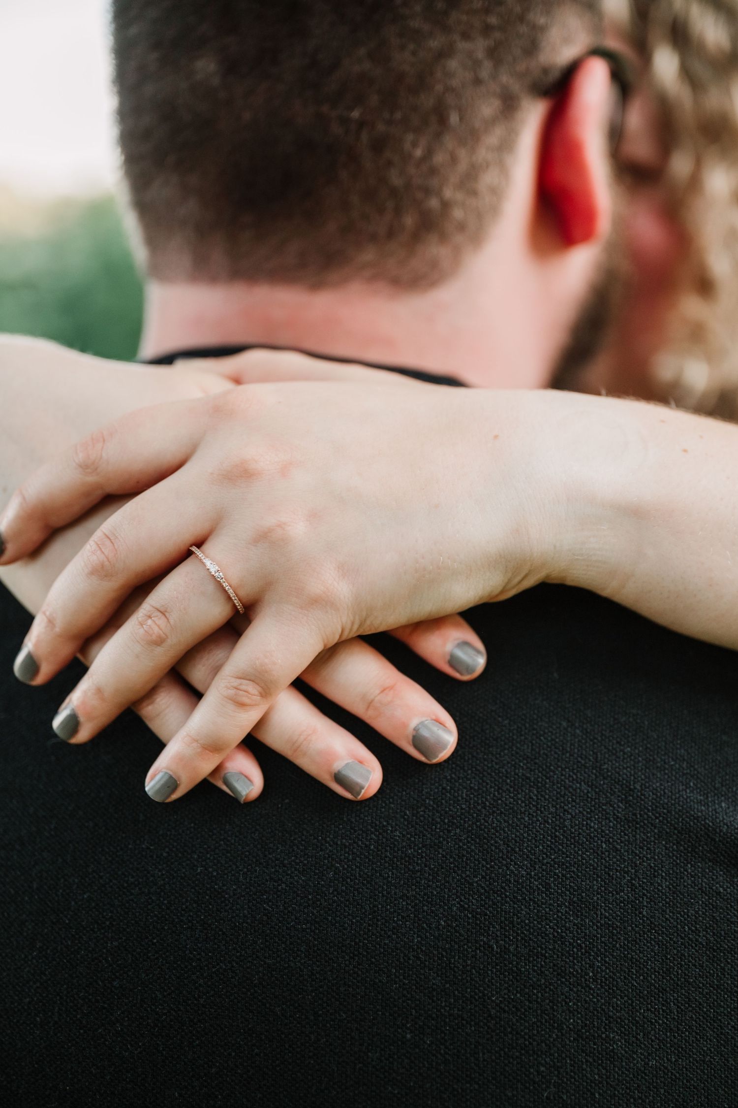 Close-up shot of hands with painted nails resting on a black shirt showing intimate connection.