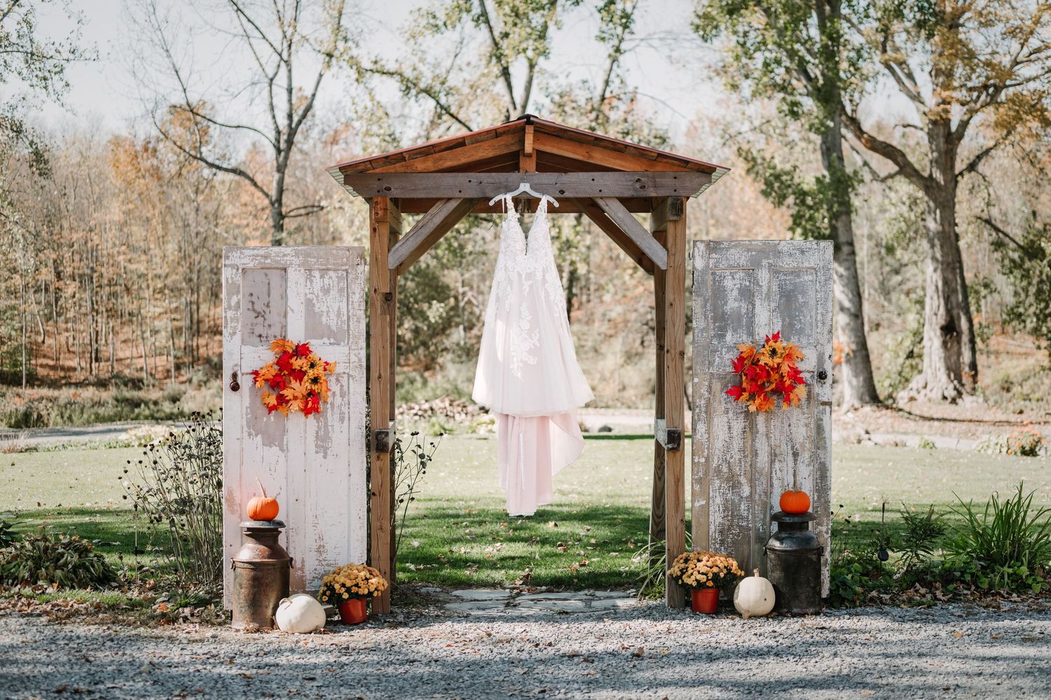 Rustic wedding arch decorated with orange flowers and white dress hanging in center.