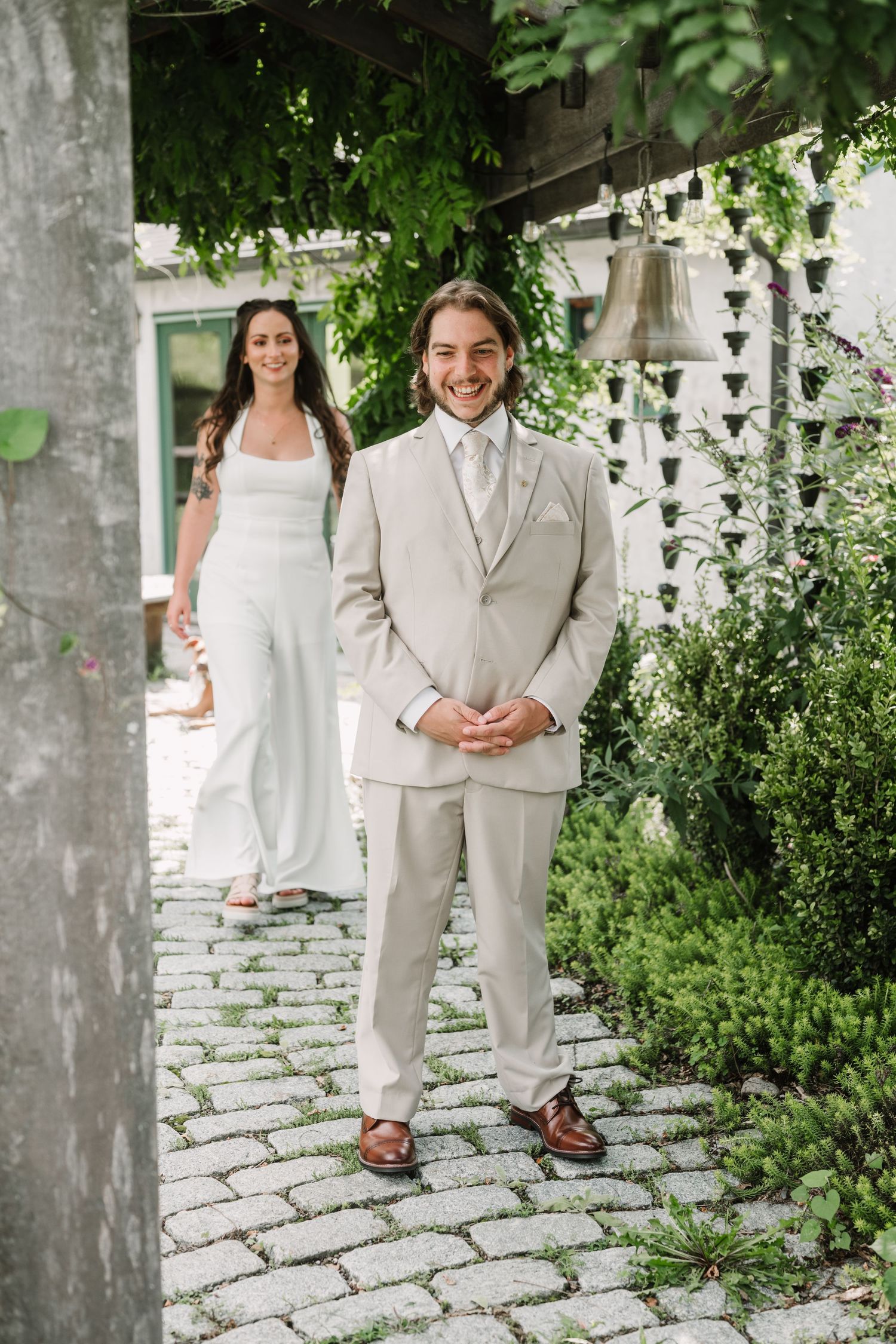 Wedding couple walking along a stone path surrounded by lush greenery and white fencing.