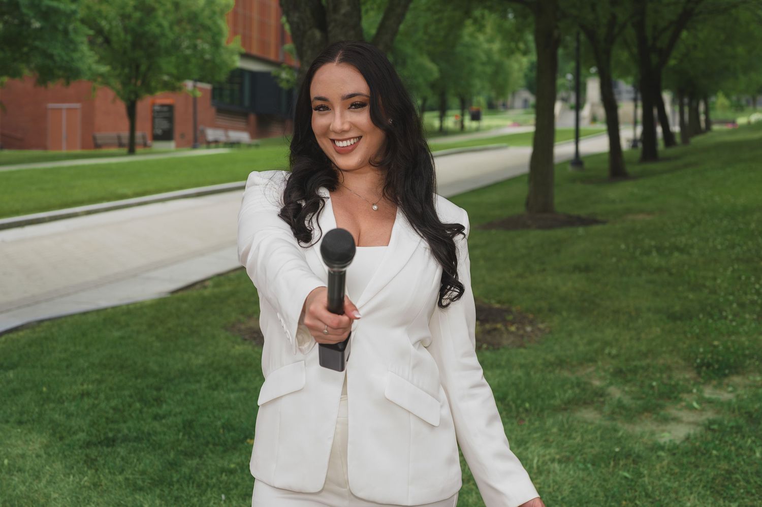 Graduate in white outfit posing for photos on university campus.
