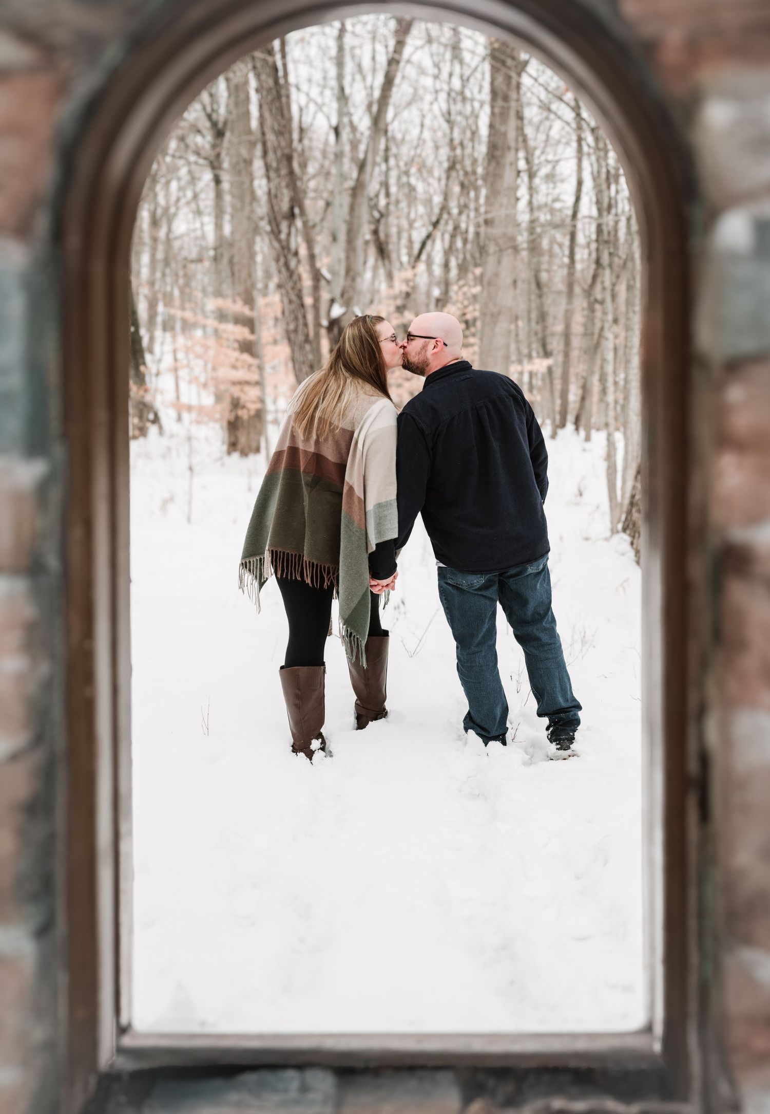 Family silhouettes framed through stone archway in snowy winter landscape.