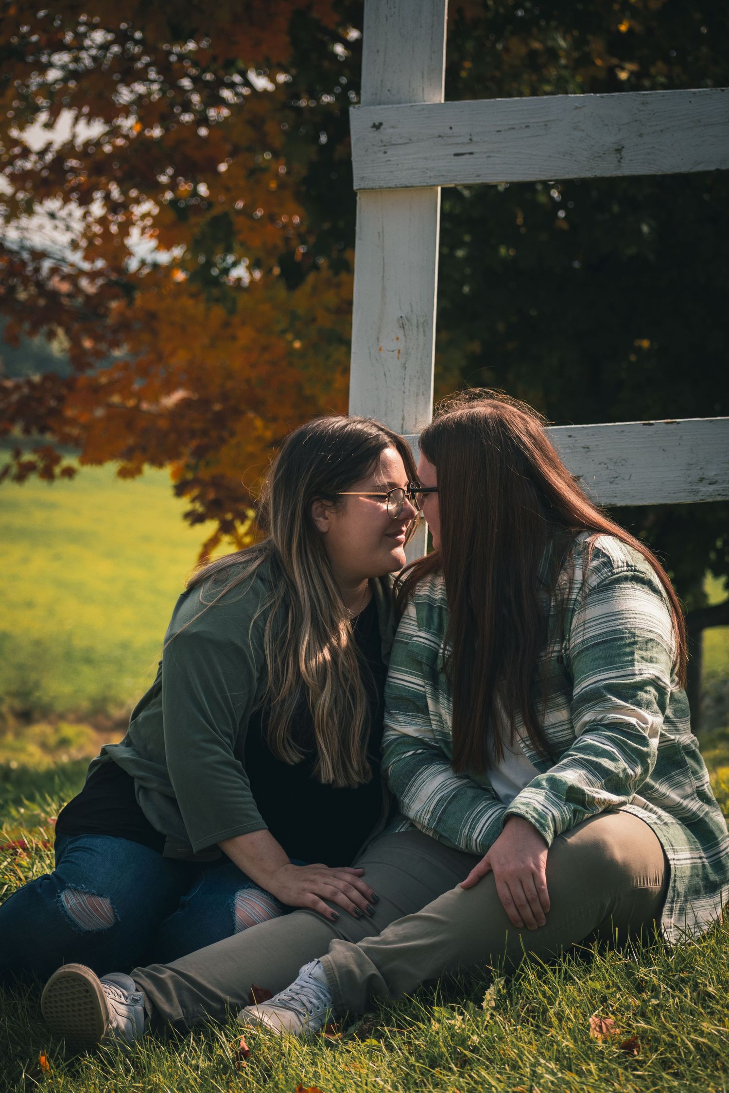Couple lying on grass near wooden fence during autumn photoshoot.