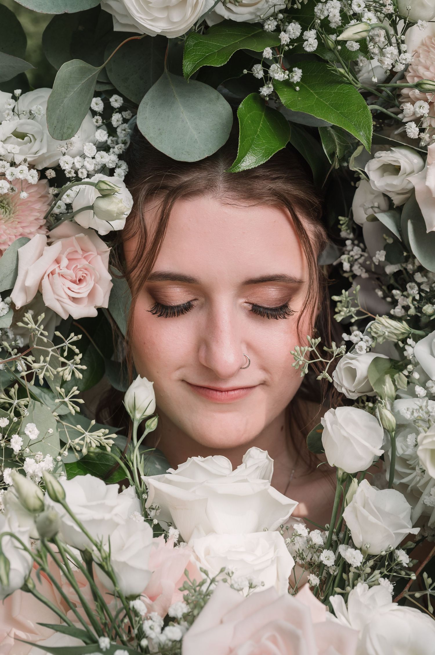 Ethereal portrait surrounded by soft pink roses, white flowers, and eucalyptus leaves.
