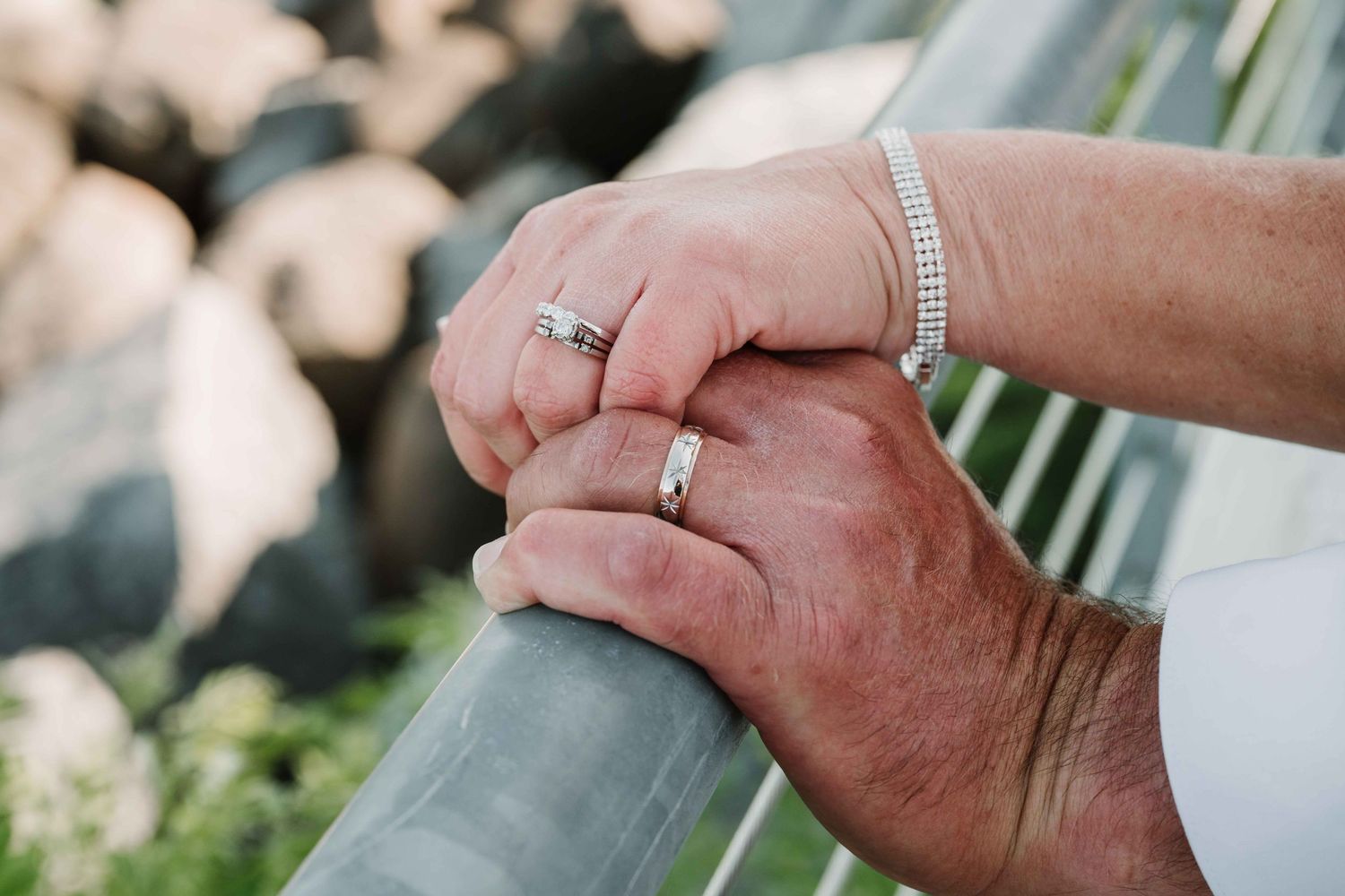 Close-up of hands with wedding ring and bracelet resting on metal railing.
