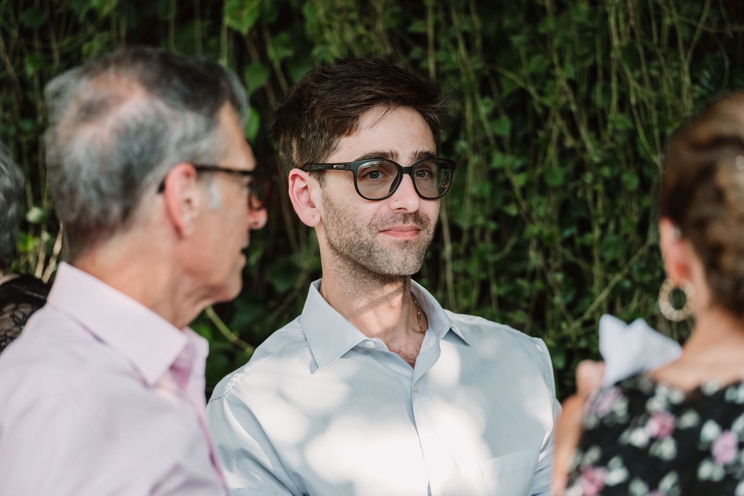 Guests share a candid moment during an outdoor wedding reception with greenery in the background.