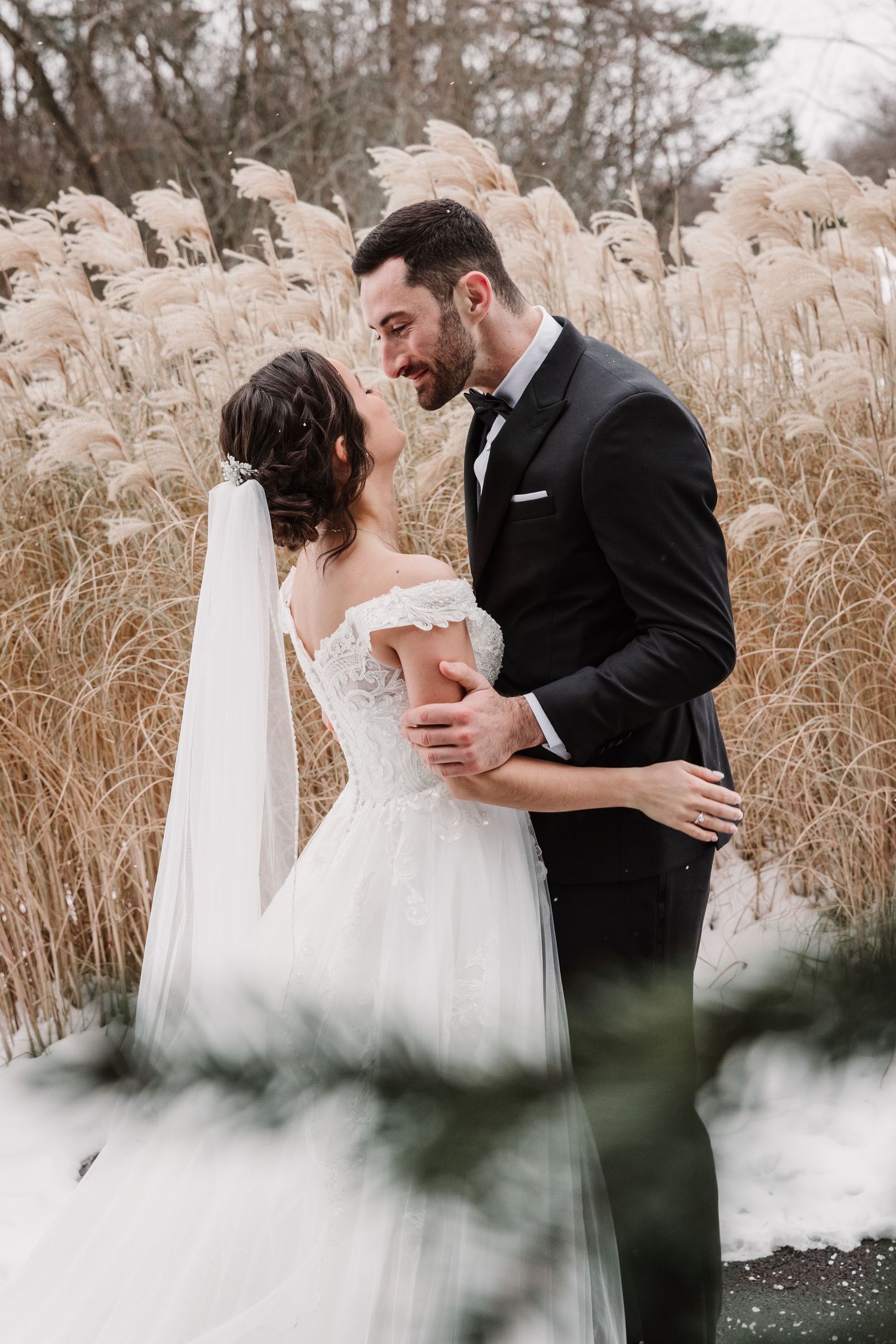 A couple shares an intimate moment among tall dried grasses in a winter landscape.