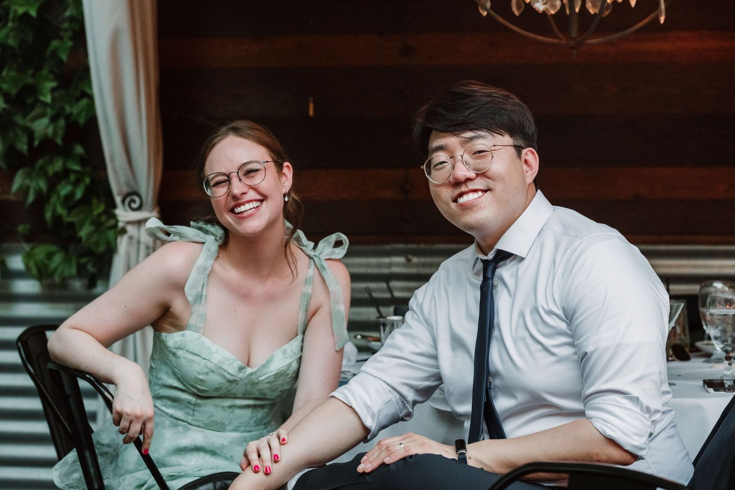 A couple shares a lighthearted moment at their wedding reception while seated.