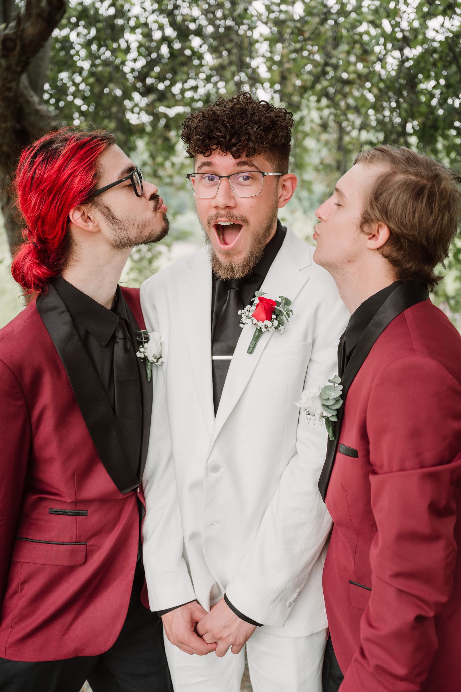Wedding party members in burgundy and white suits share candid laughing moments outdoors.