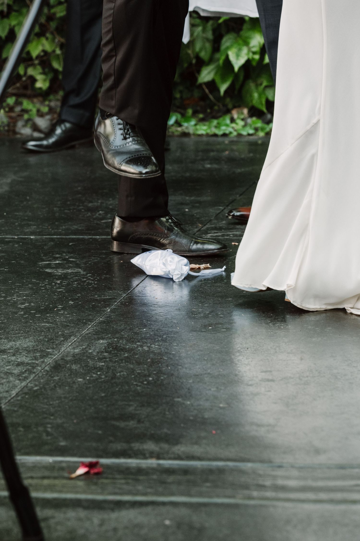 Detail shot of formal shoes and white dress hem on dark floor at wedding.