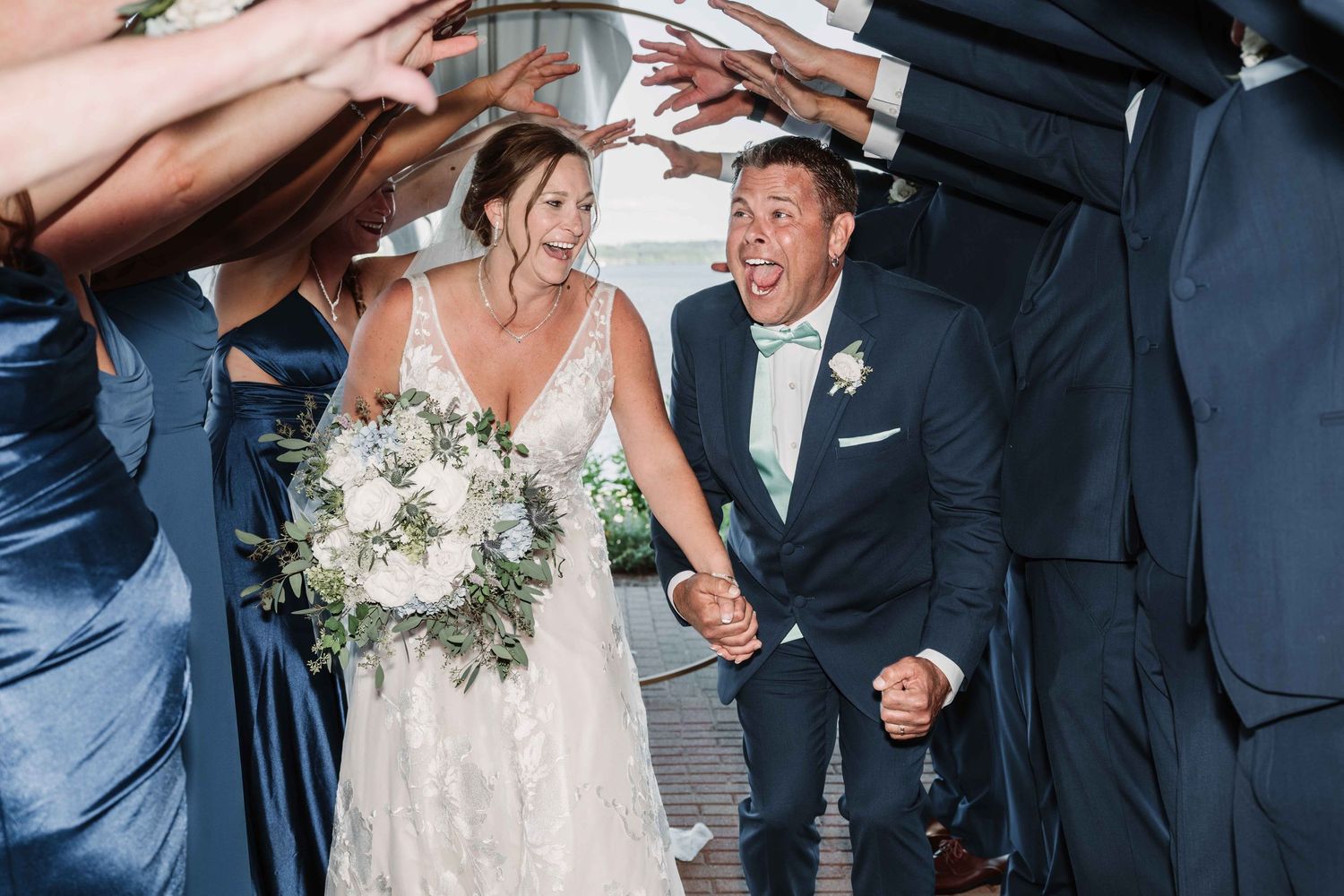 Newlyweds share joyful laughter during their outdoor wedding photoshoot by the water.