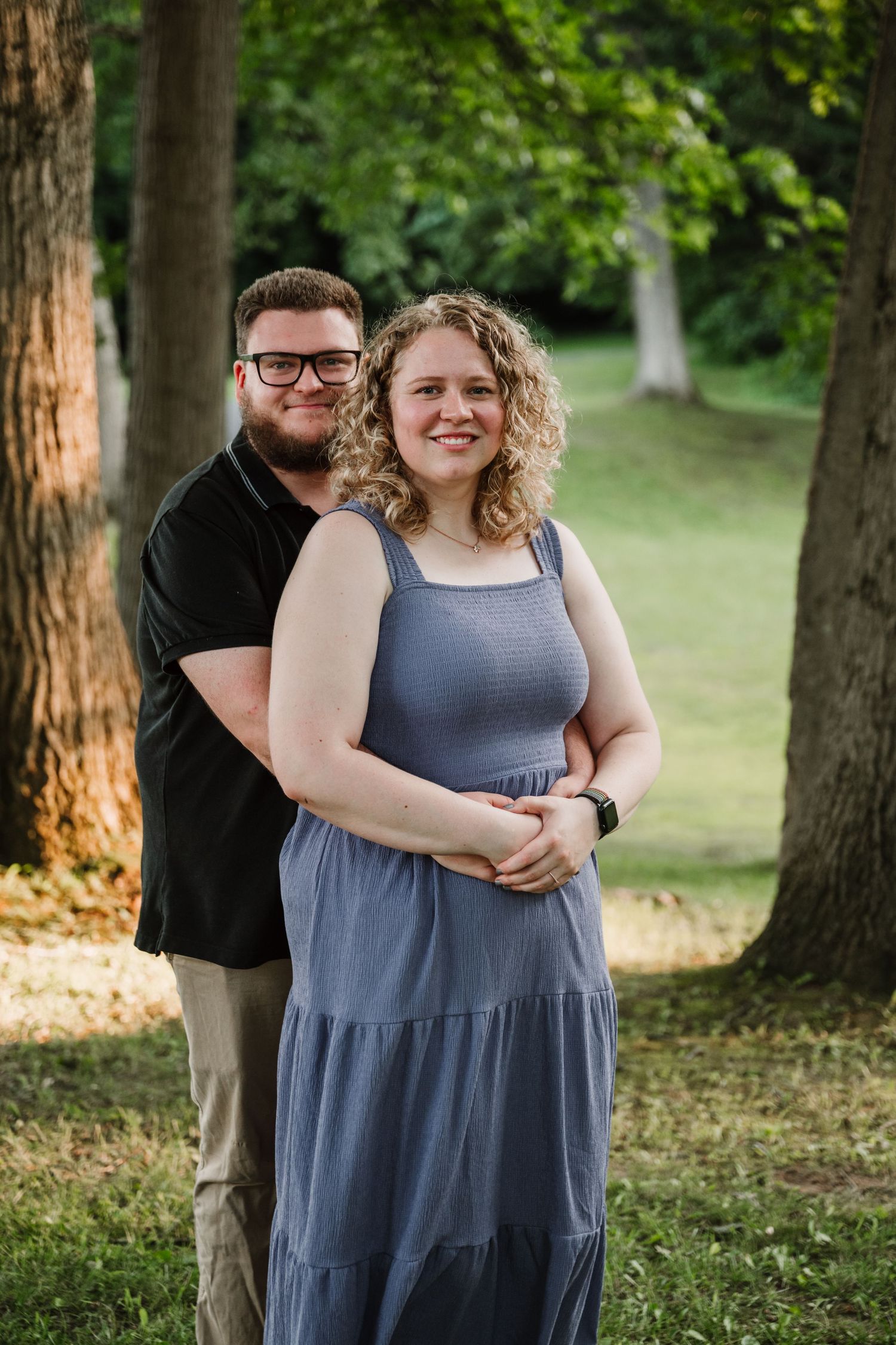 A couple laughs together during a casual outdoor photoshoot among tall trees.