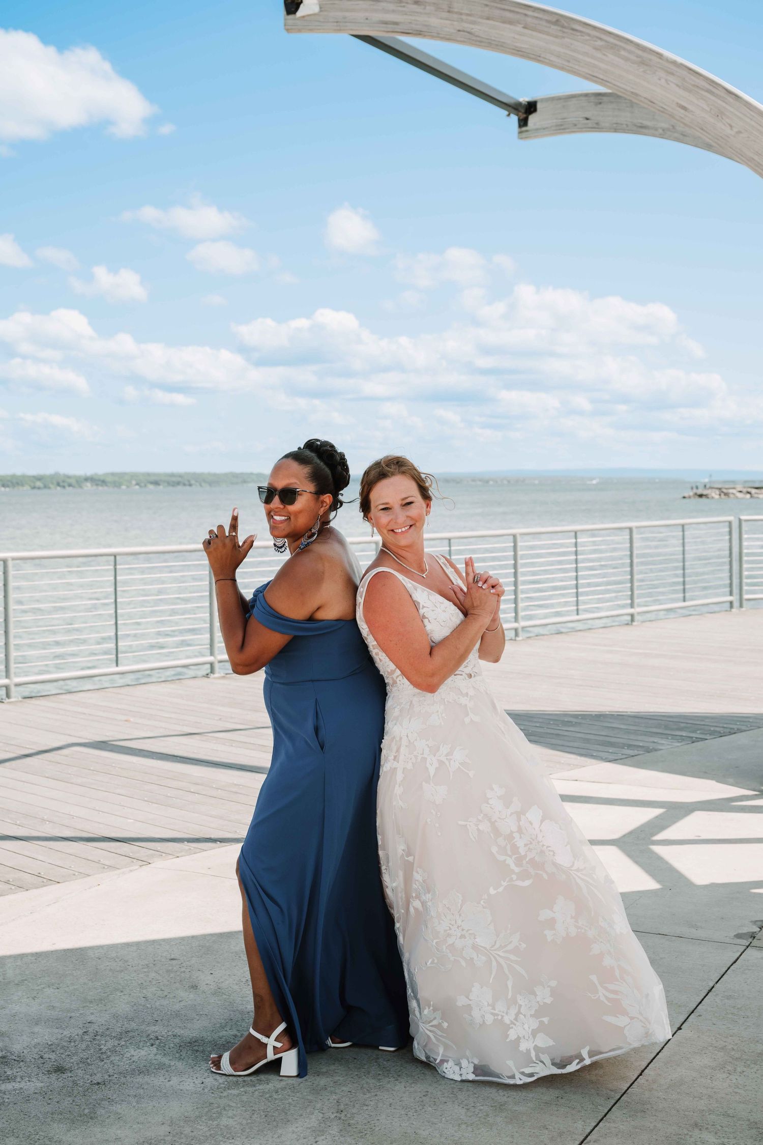 Two people in navy and white attire strike playful poses on a waterfront terrace with ocean views.