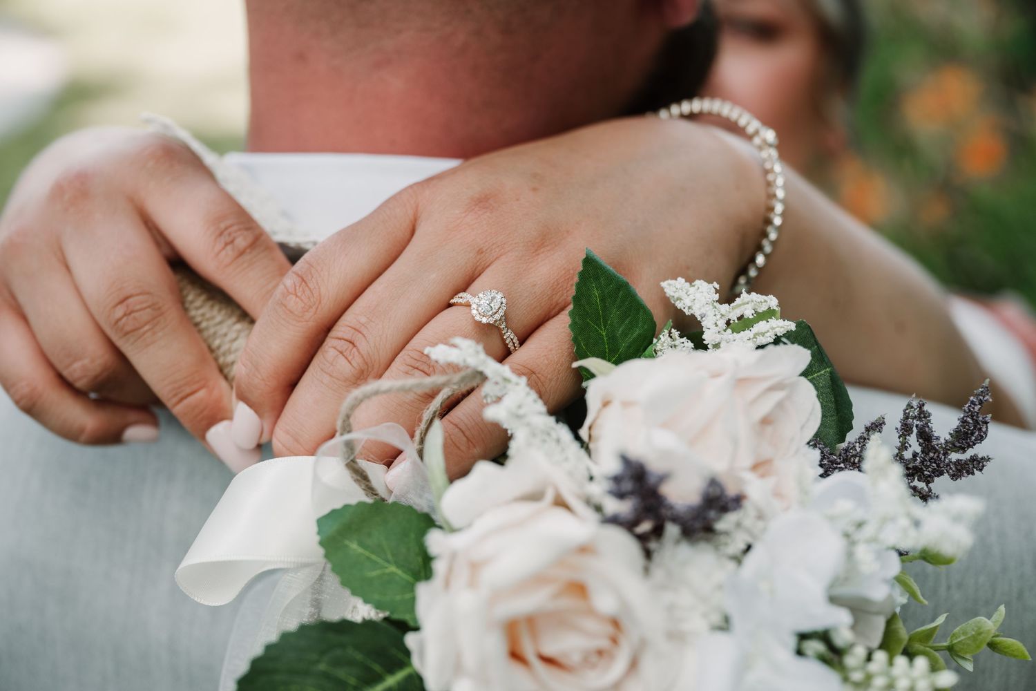Close-up of wedding rings and white roses in a delicate bridal bouquet with greenery.