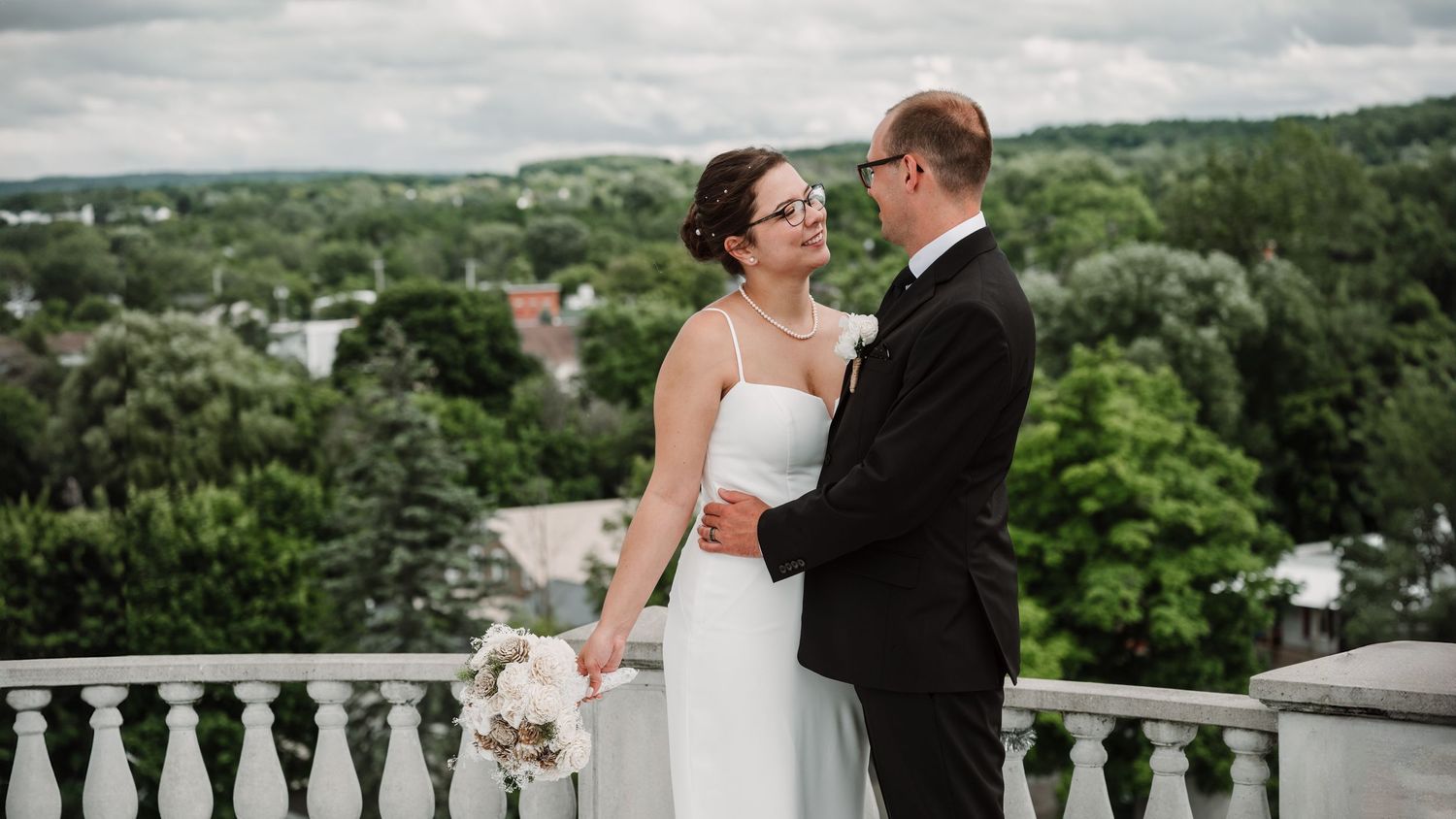 Wedding couple embracing on a scenic overlook with rolling hills in the background.