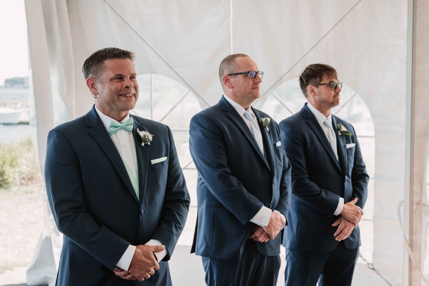 Groomsmen in dark suits stand in a row during a wedding ceremony.