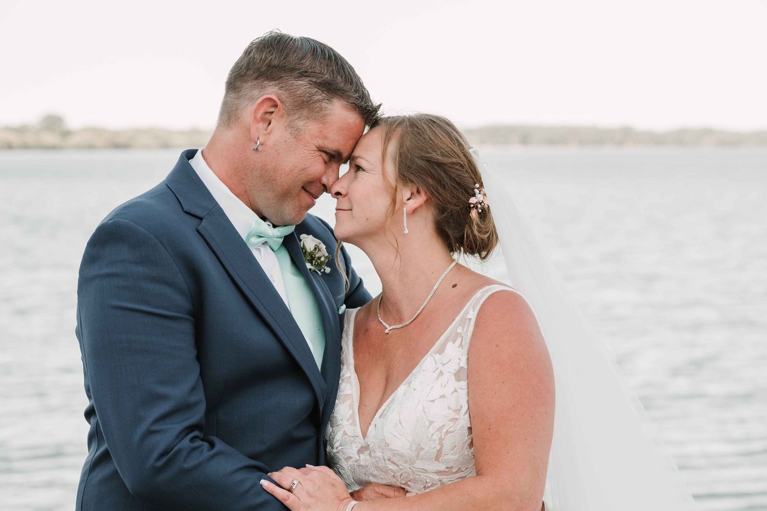 Romantic waterside wedding photos with couple sharing tender moments.