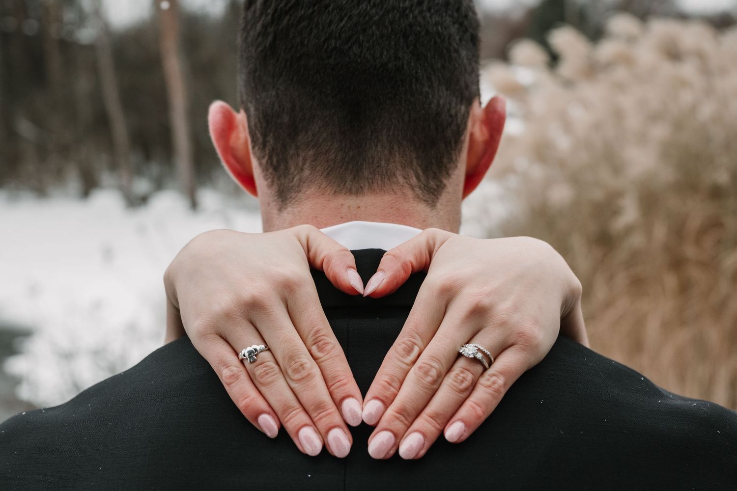 Close-up of hands wearing wedding rings embracing from behind.