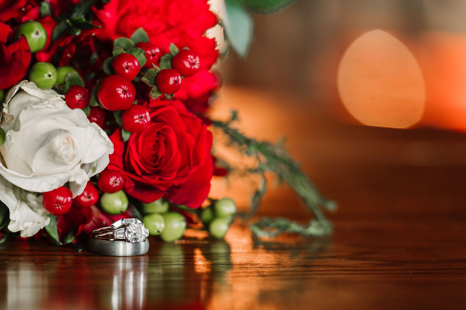 Elegant red and white rose bouquet with wedding rings on wooden surface with bokeh background.