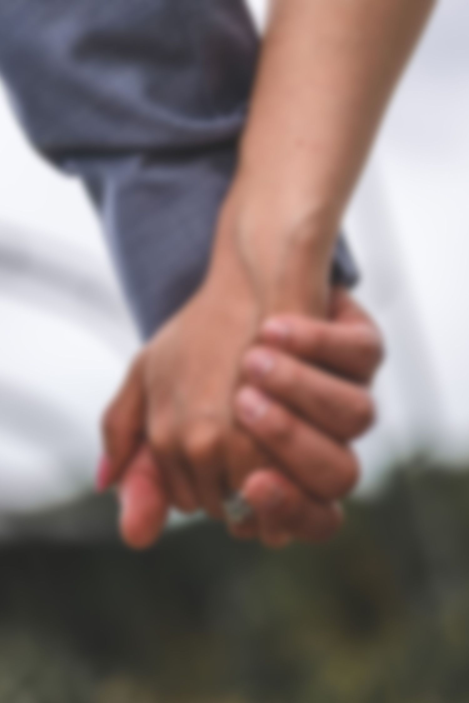 Close-up of two hands clasped together against a blurred outdoor background.
