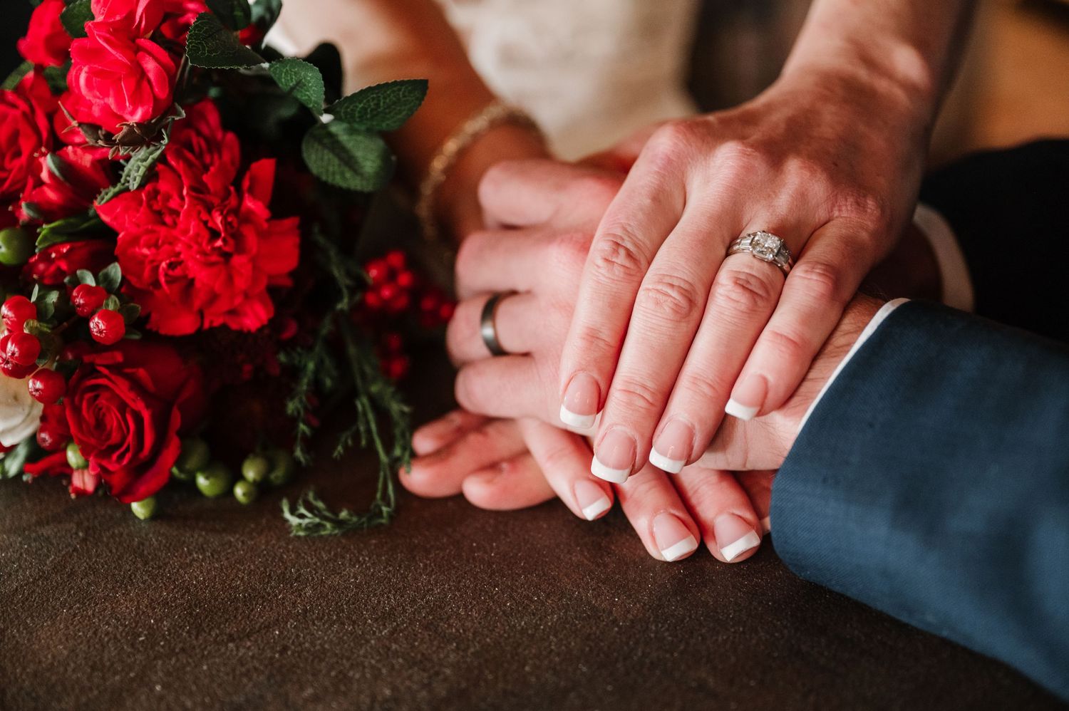 Hands with wedding rings intertwined next to vibrant red roses.