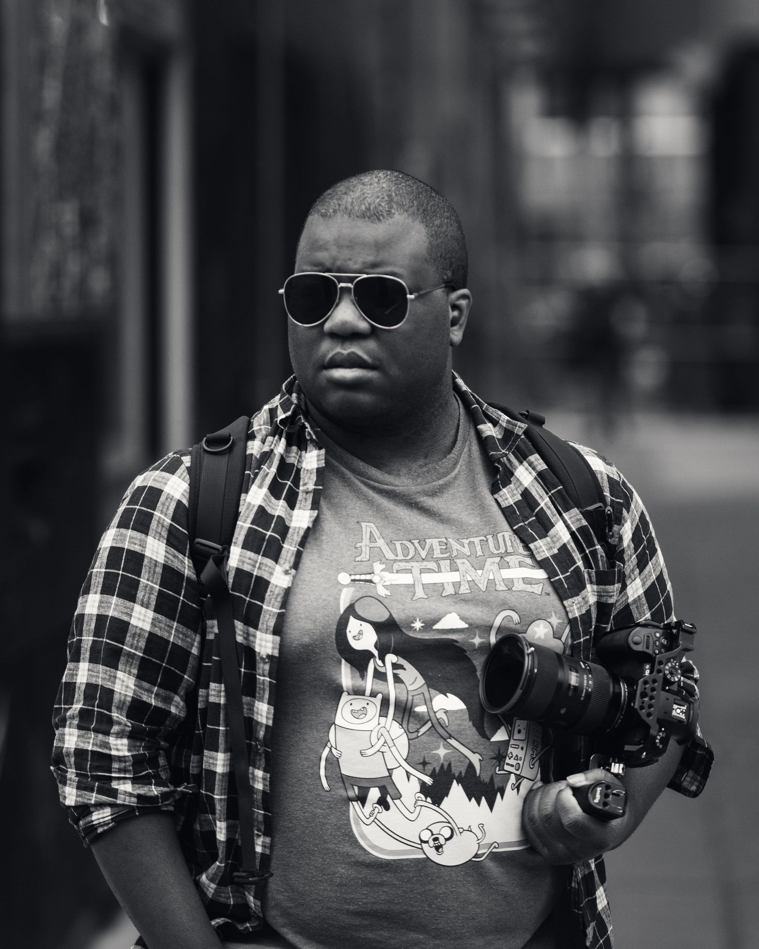 Street photographer wearing plaid shirt and graphic tee capturing urban scenes.