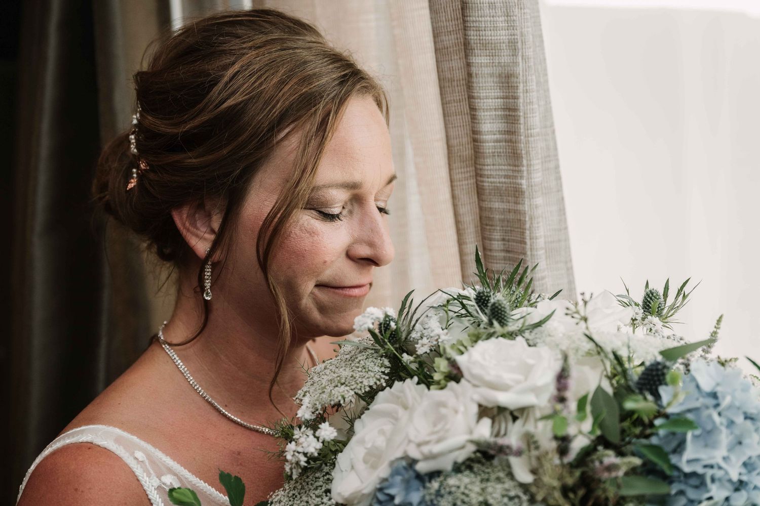Bride with updo hairstyle admiring white and blue wedding bouquet.