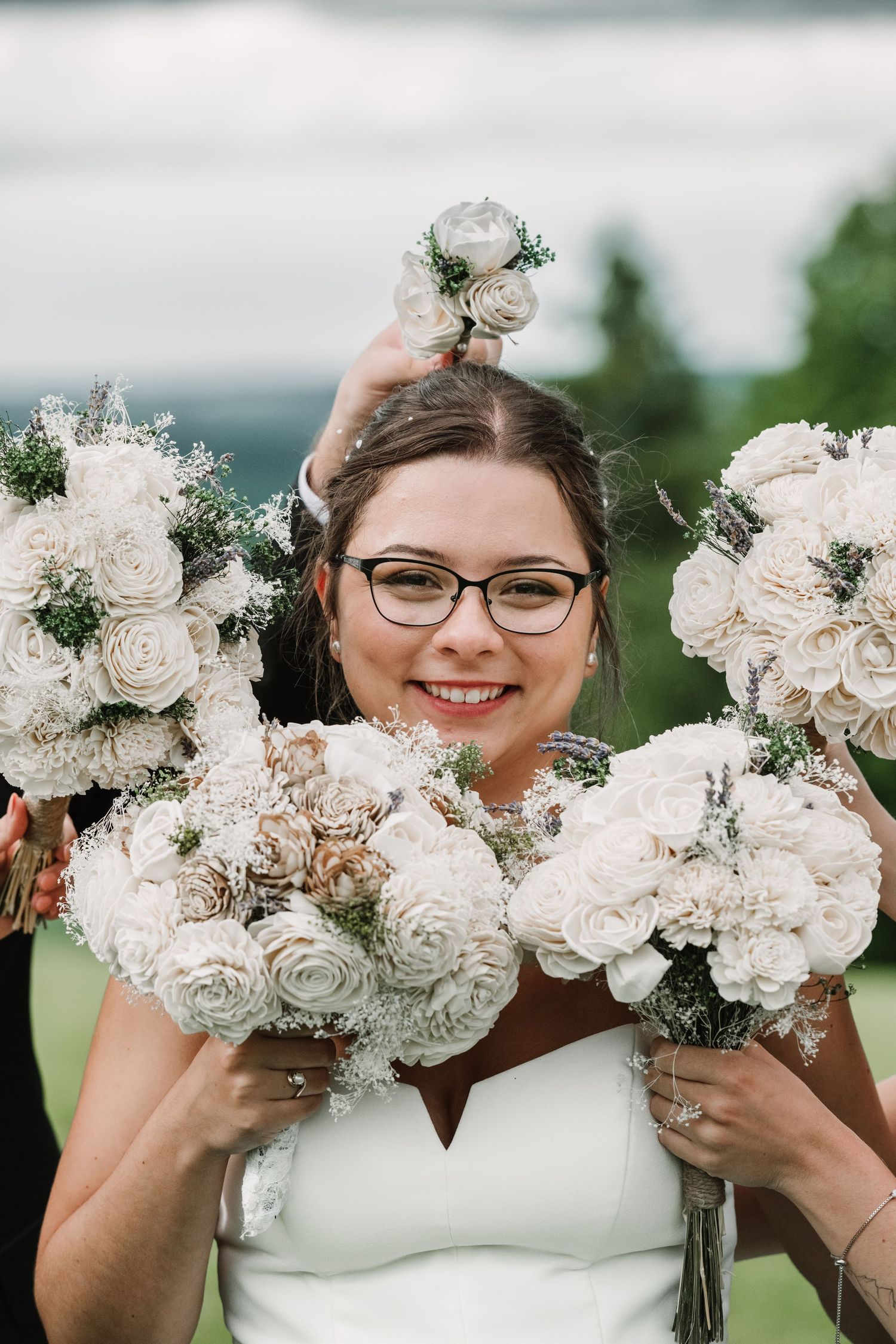 Smiling bride in glasses surrounded by white sola wood flower bouquets on her wedding day outdoors.