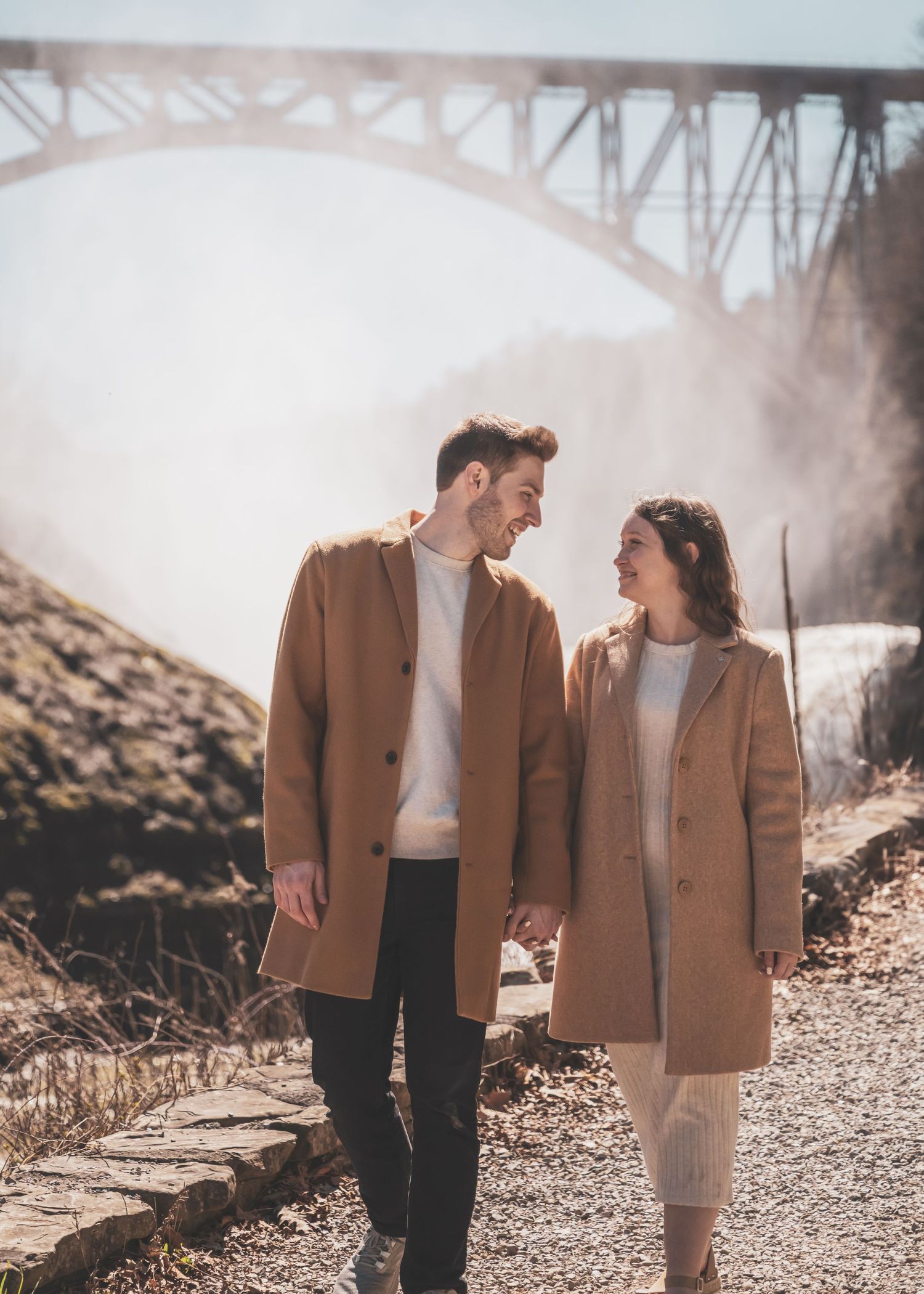 Romantic couple walking and embracing on a rocky path beneath a bridge.