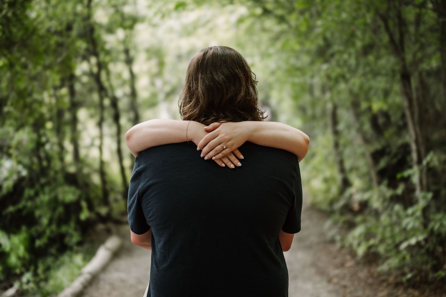 A couple shares an intimate moment while walking through a lush green forest path.