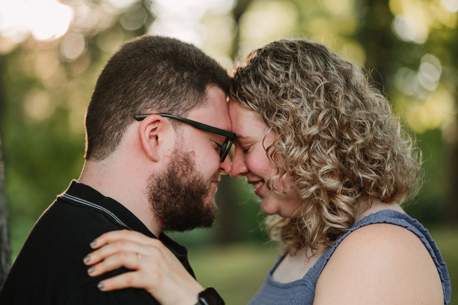 A couple shares a tender moment in a sunlit park during golden hour.