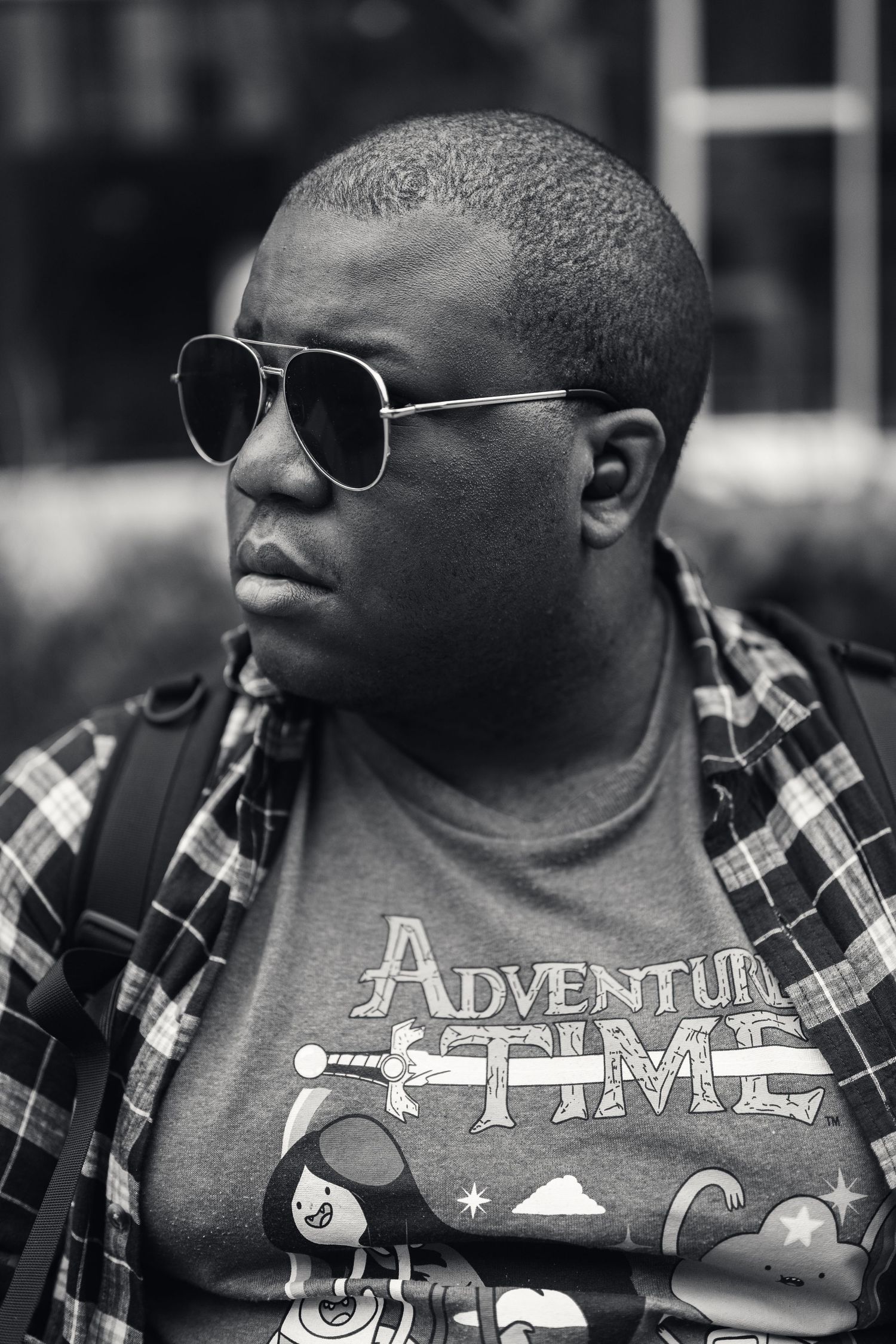 Street photographer wearing plaid shirt and sunglasses in urban setting.