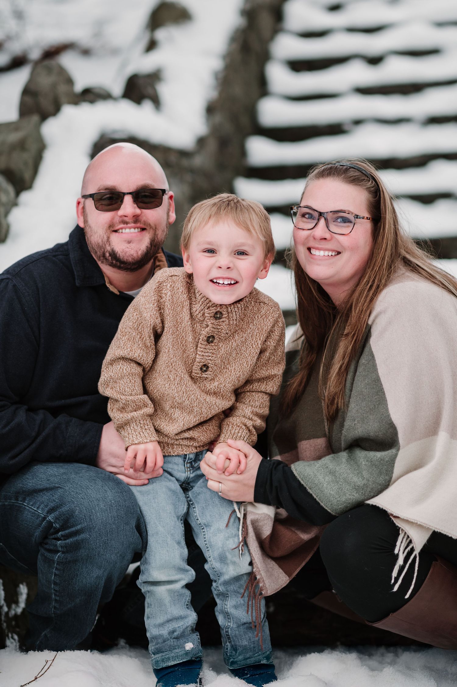 Happy family sitting together on snowy steps during winter photoshoot.