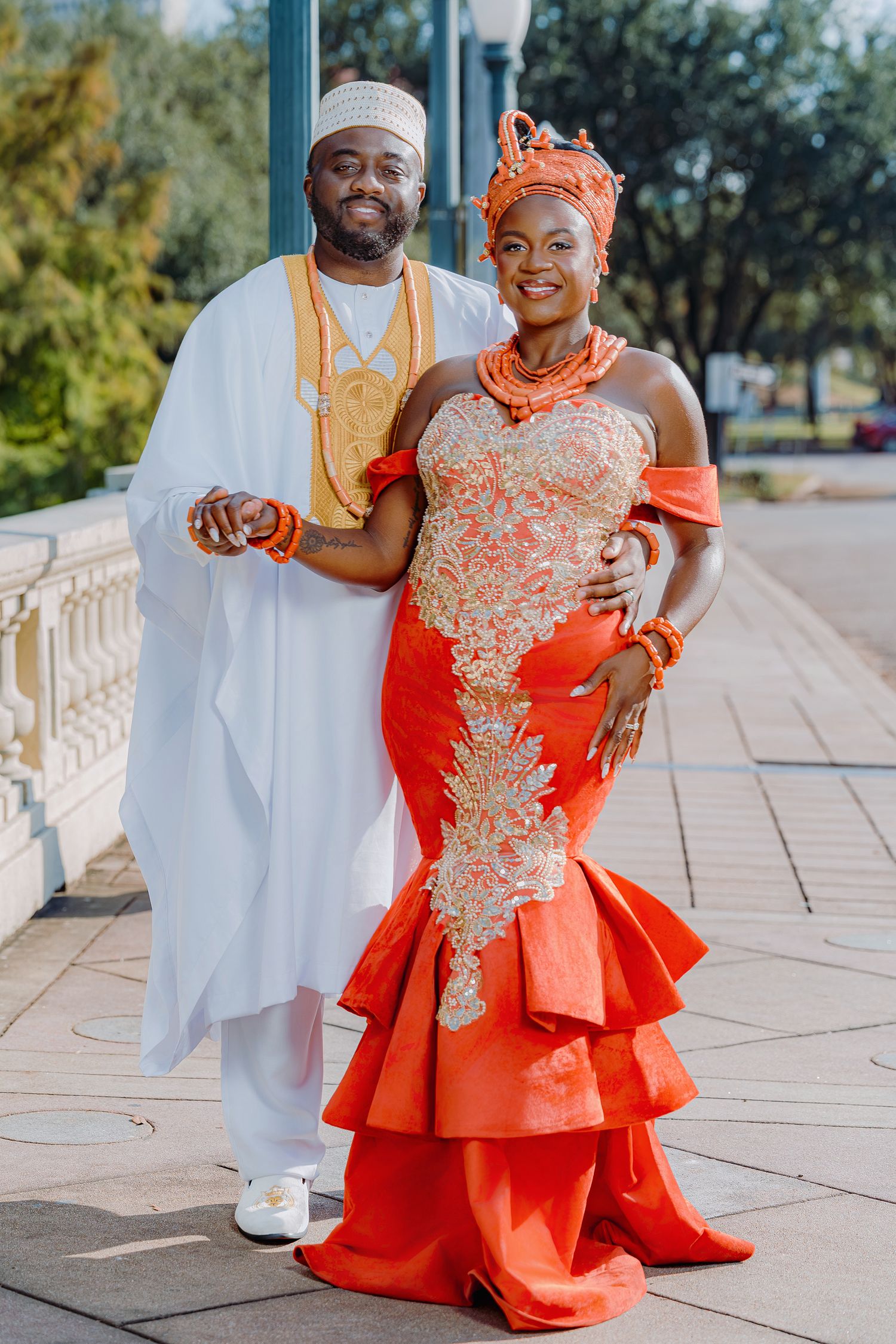 A couple in traditional wedding attire poses together, with the bride wearing an elegant orange dress with gold embellishments.
