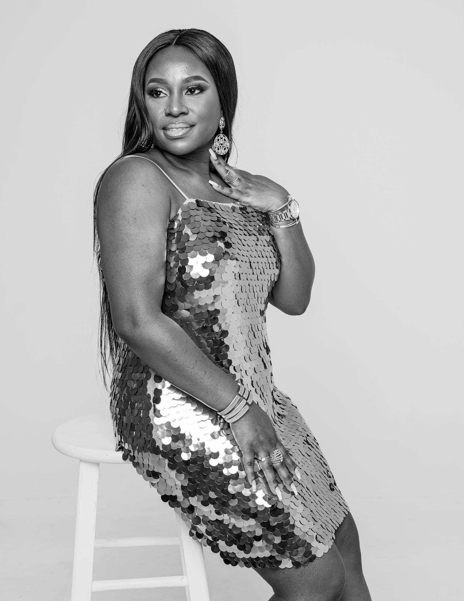 A glamorous figure in a sparkling silver sequined bodysuit poses confidently against a white backdrop in a series of shots.