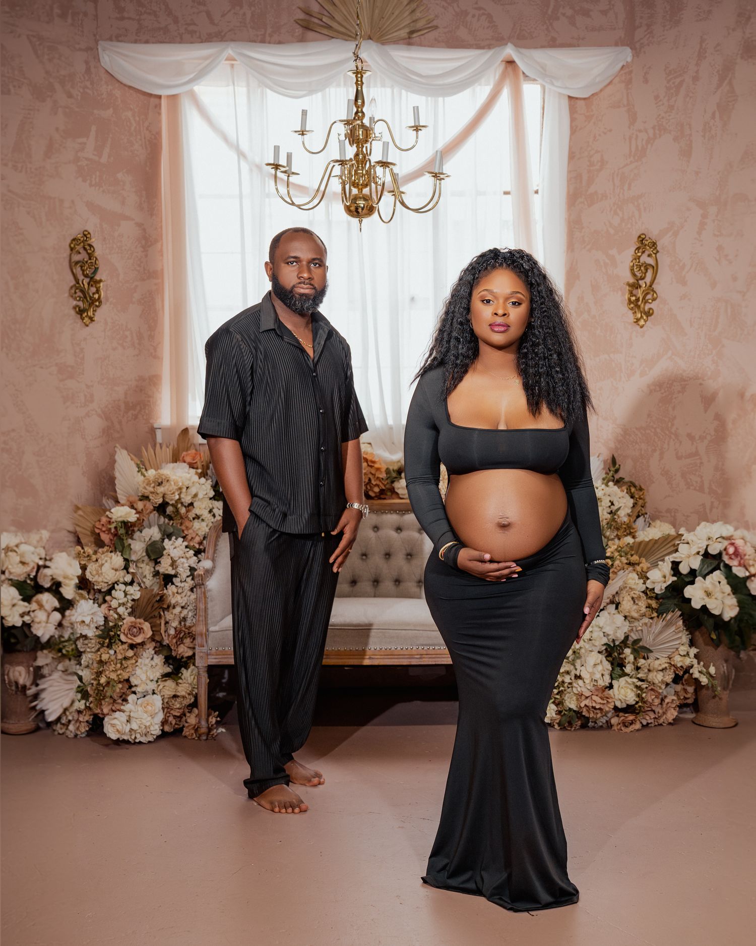 Maternity photo shoot in elegant room with gold chandelier, white floral arrangements and pink walls.