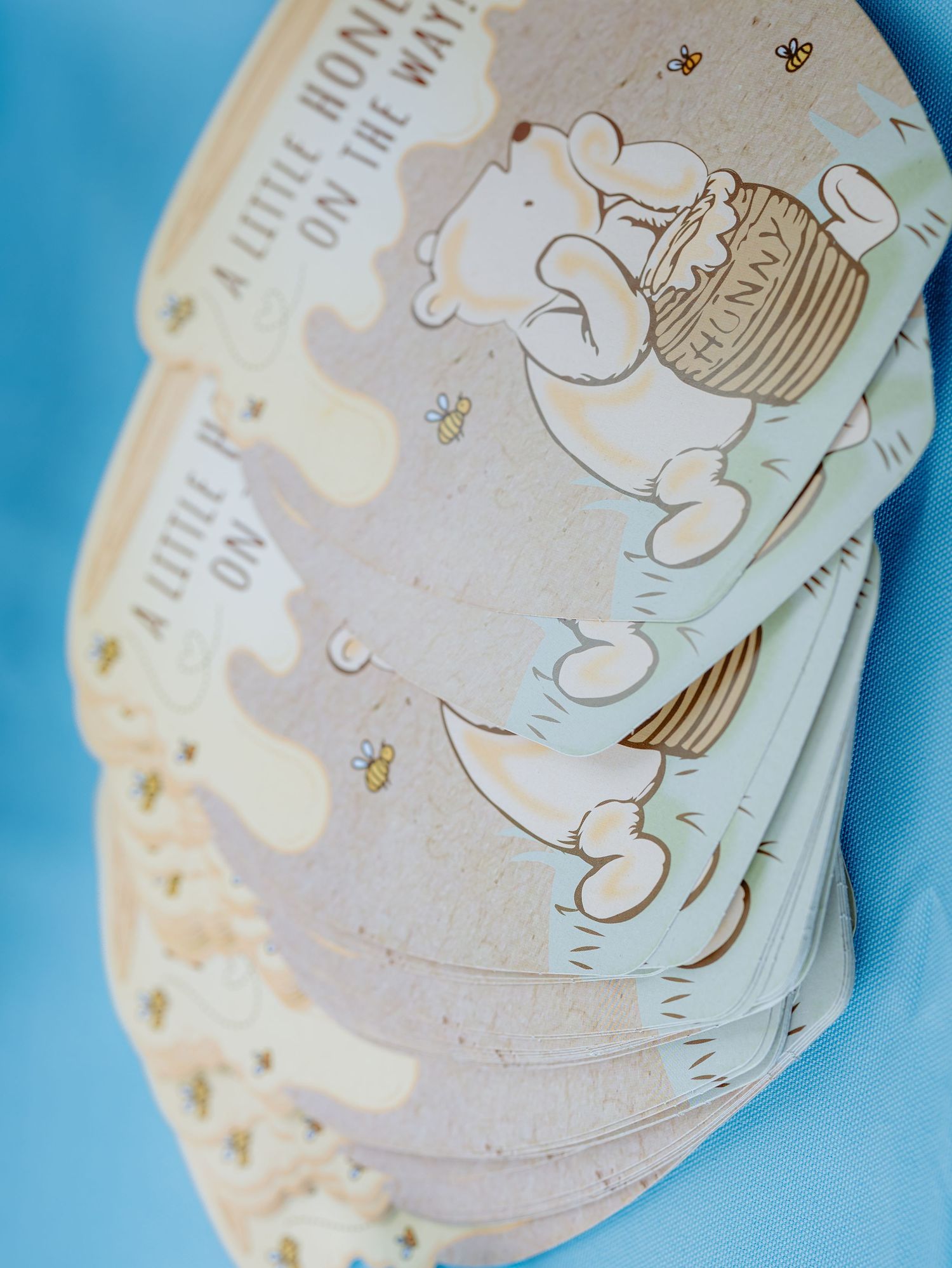 A stack of curved paper cards with cute bear illustrations and honey bee designs on a blue background.