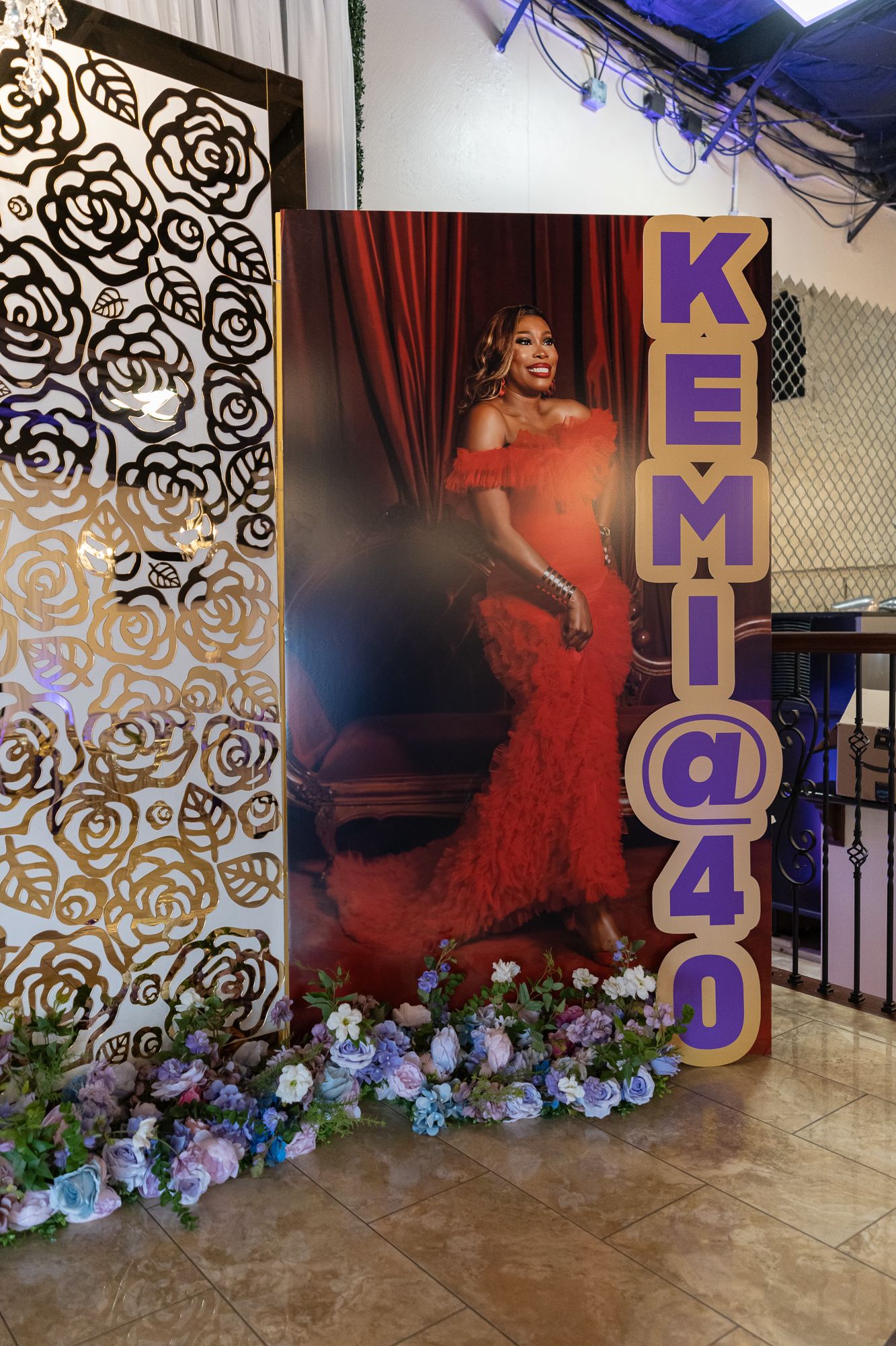 Elegant photo backdrop with gold floral patterns, purple lighting, and blue hydrangea flowers arranged at the base.