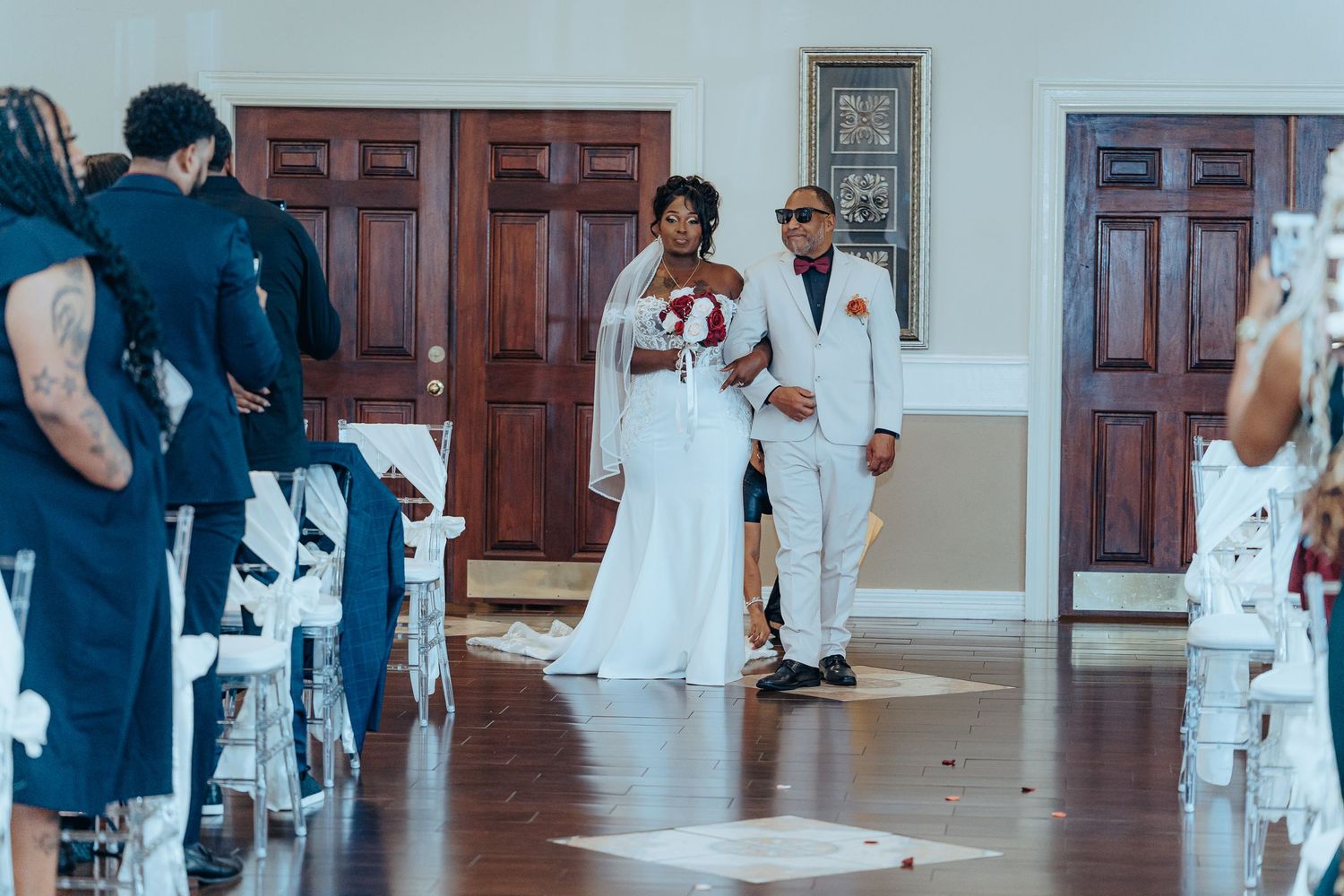 Wedding party members gather in formal attire inside an elegant venue hall.