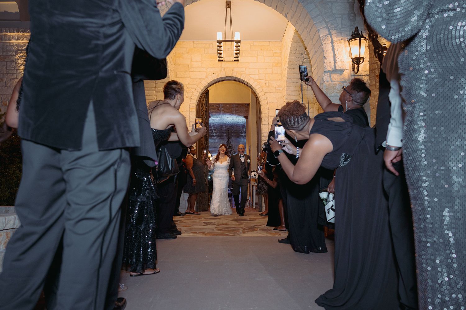 A wedding party walks through an arched hallway decorated with lanterns and elegant lighting.