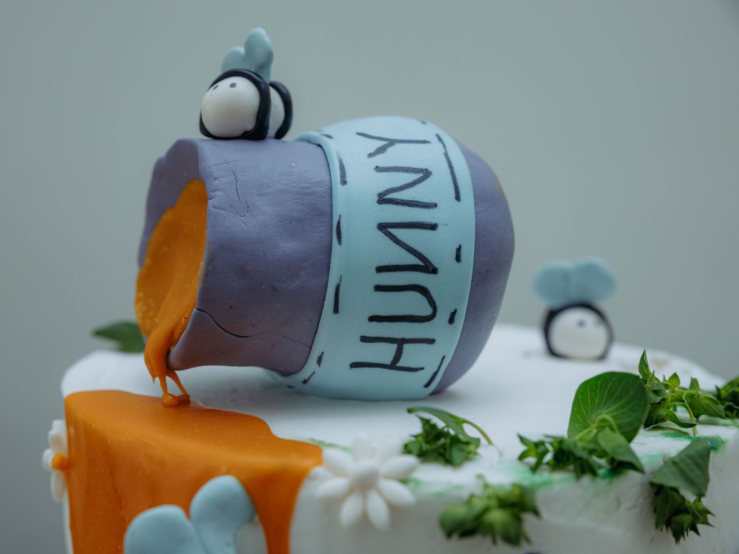 A whimsical cake decorated with a spilled Winnie the Pooh honey pot design, dripping orange honey and green foliage.