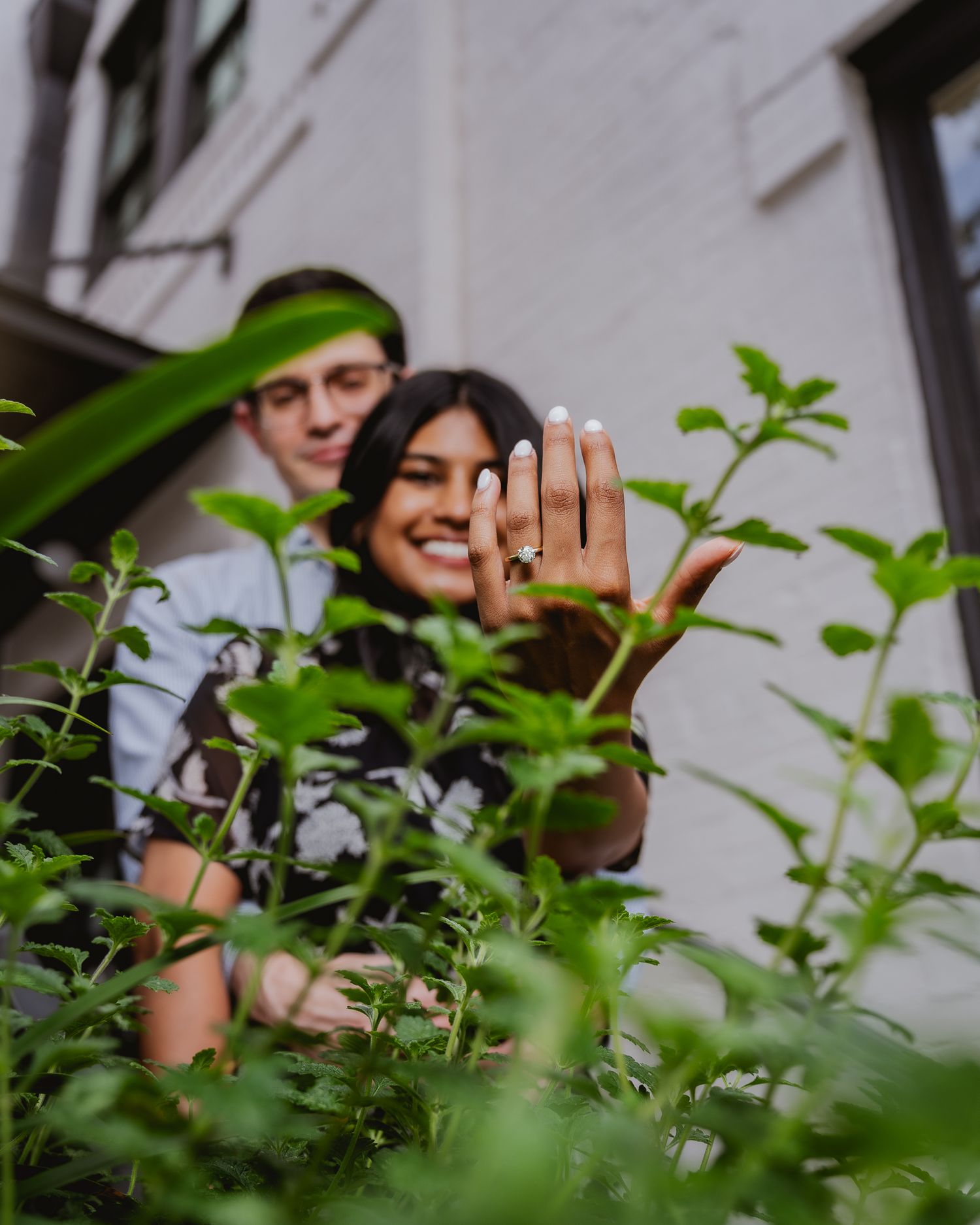 Green plants frame an engagement photo session with soft natural lighting.