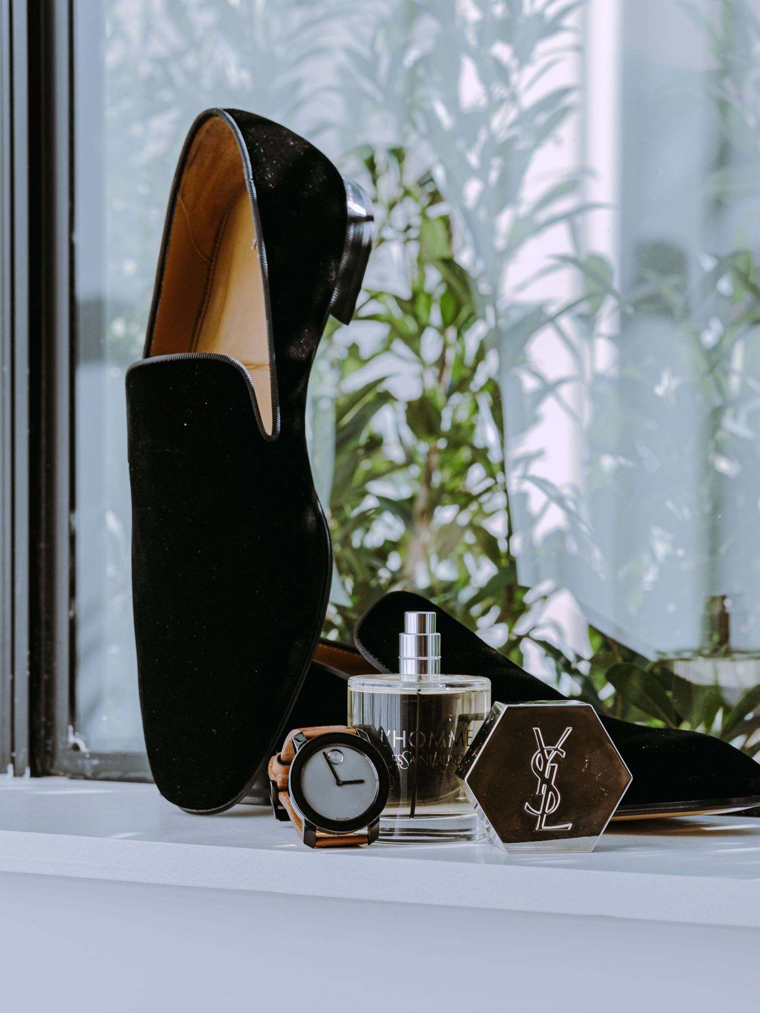 Black velvet loafer with YSL perfume bottle and watch on white windowsill.