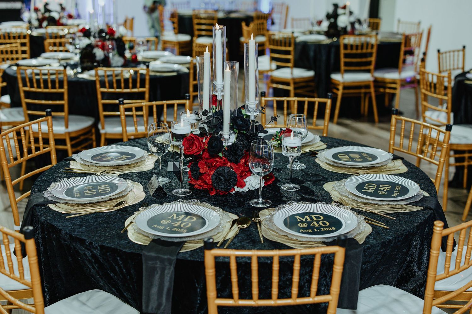 Elegant wedding reception table with black tablecloth, red roses, silver candles and gold chiavari chairs.