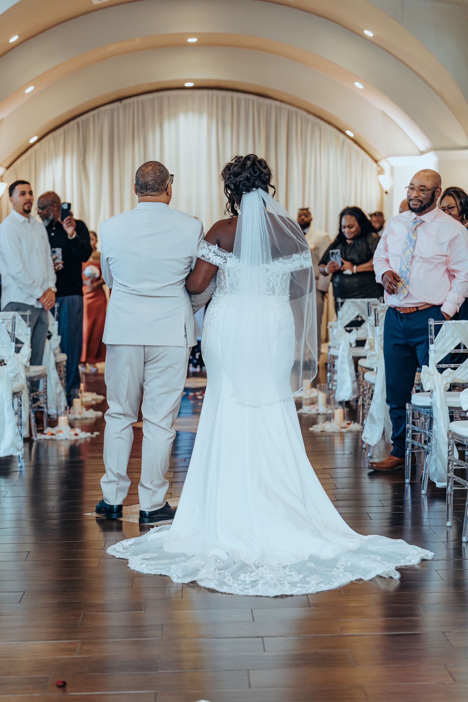 Wedding reception guests dance and celebrate together on a polished hardwood floor under arched ceilings.