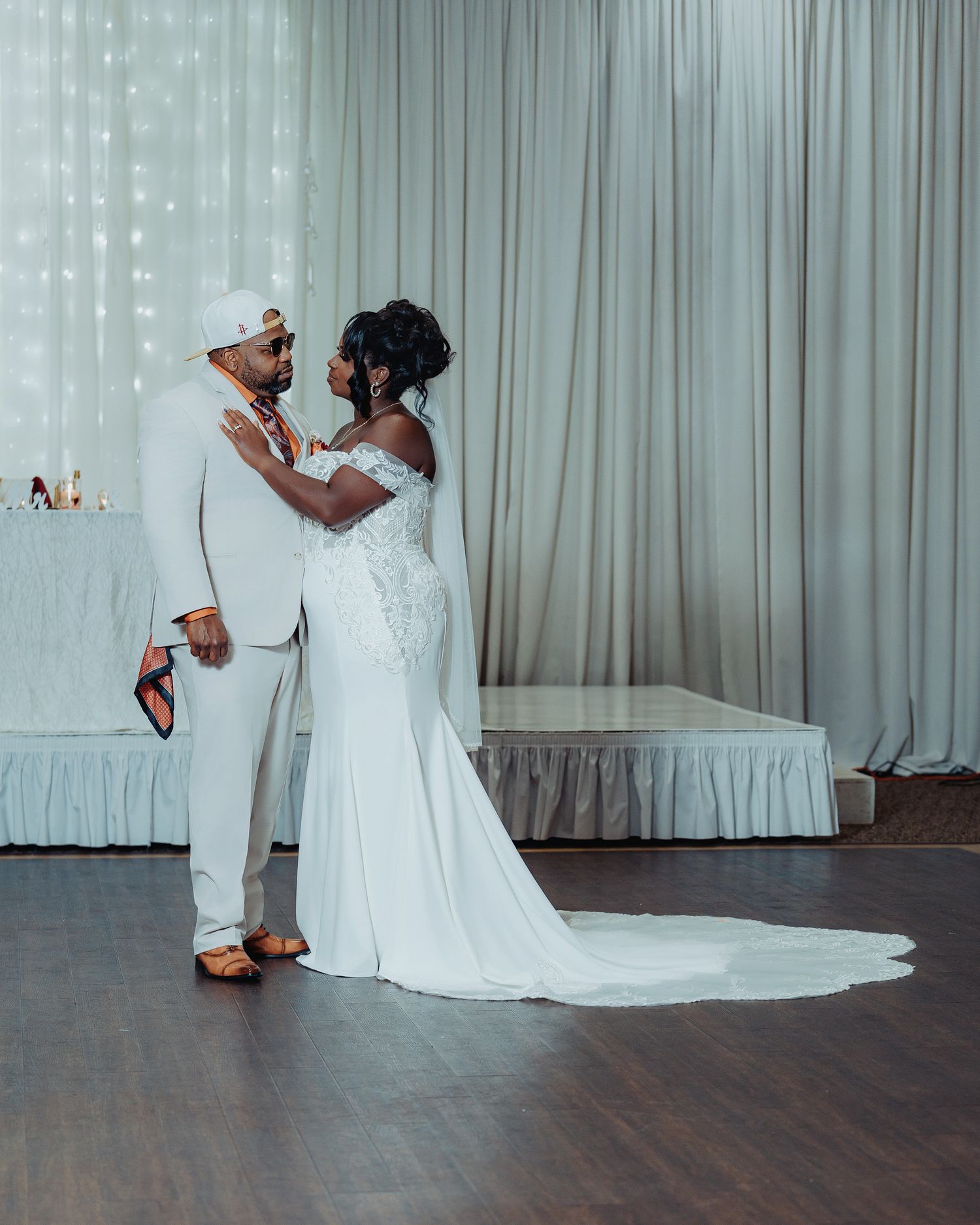 Wedding couple dancing in an elegant white reception room with flowing curtains.