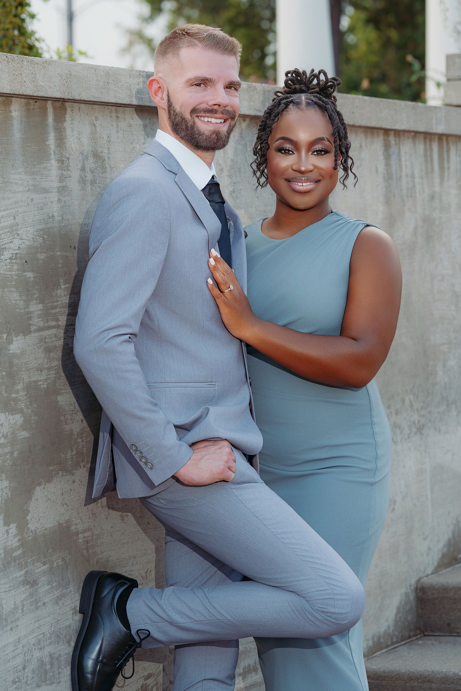 A couple wearing matching gray and blue outfits pose together against a concrete wall in an outdoor setting.